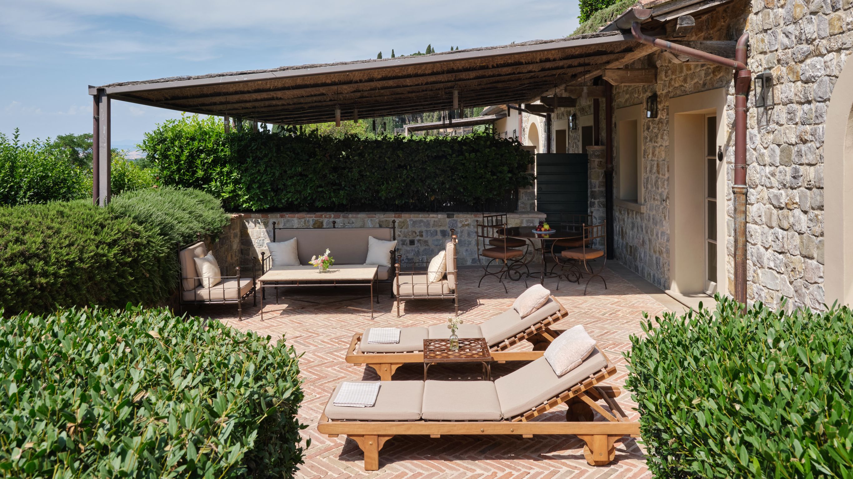 Outdoor patio with lounge chairs, sofa, tables,  and greenery
